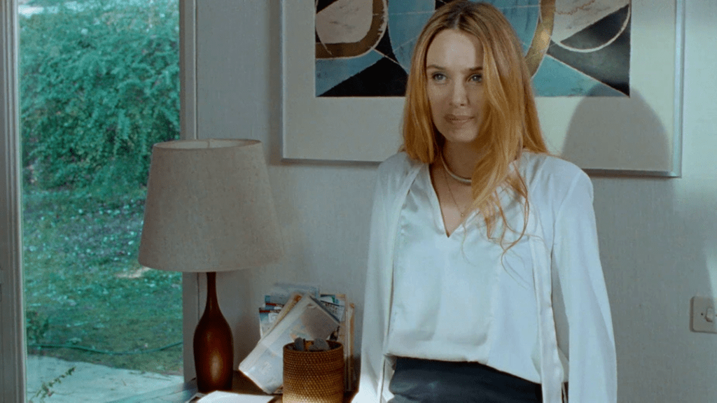 Hélène (Laetitia Dosch) leaning against a desk, smiling.