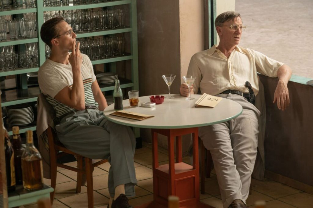 Allerton (Drew Starkey) and Lee (Daniel Craig) having drinks together in a bar, Lee looking disheveled and carrying a gun in his belt. 
