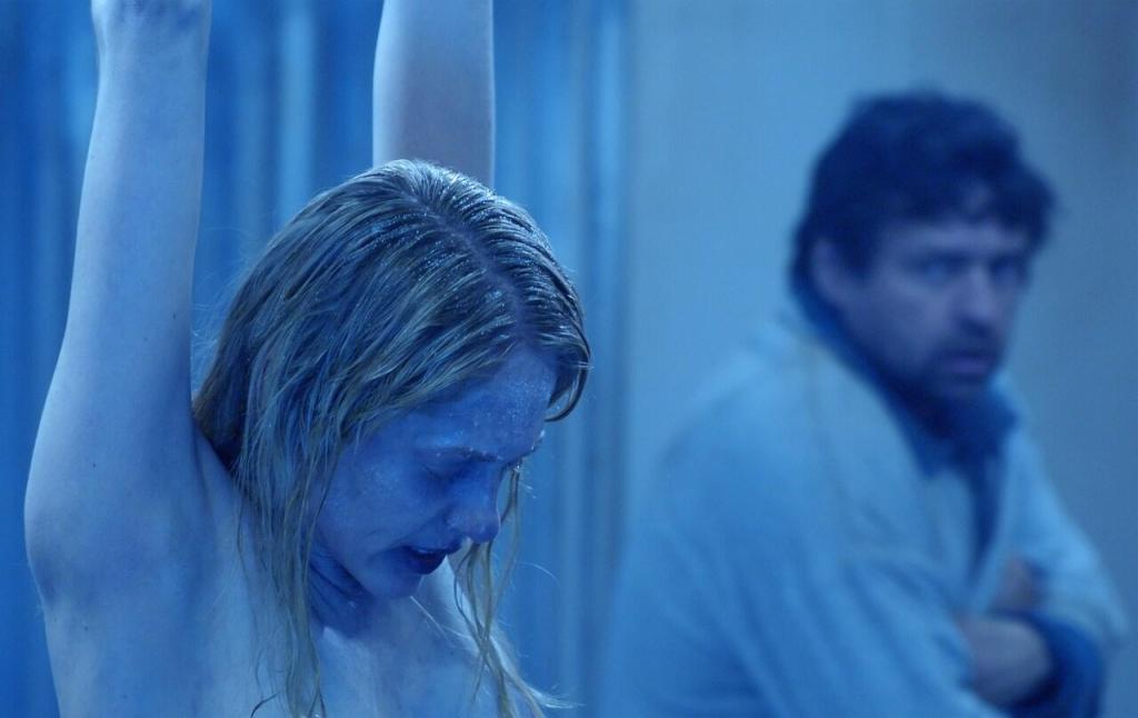 Jeff (Angus Macfadyen) standing behind a frozen naked corpse.