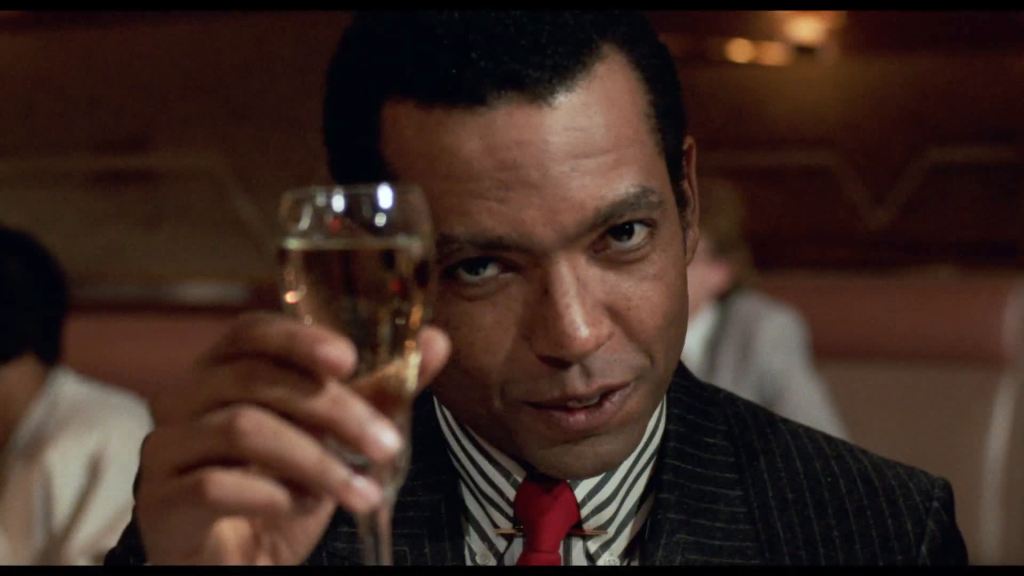 William Douglas Street Jr. (Wendell B. Harris Jr.) raising a champagne glass, looking directly at the camera. 