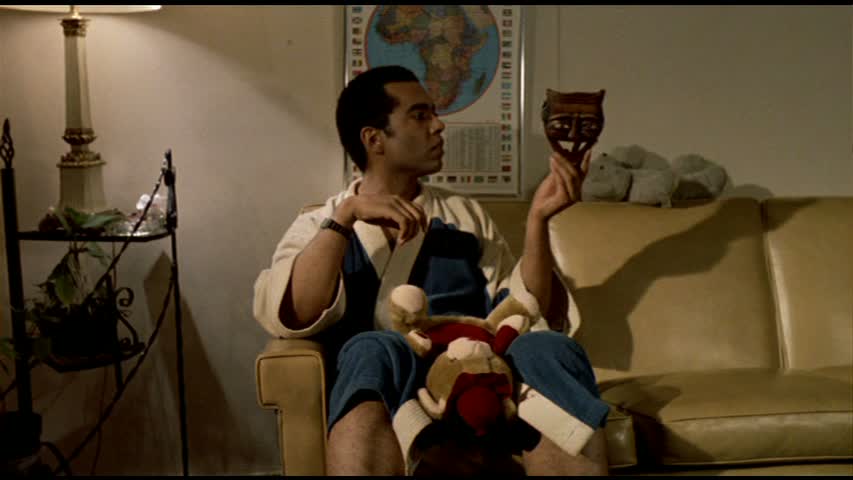 William Douglas Street Jr. (Wendell B. Harris Jr.) sitting on a sofa in bathrob, holding up a devil mask. 