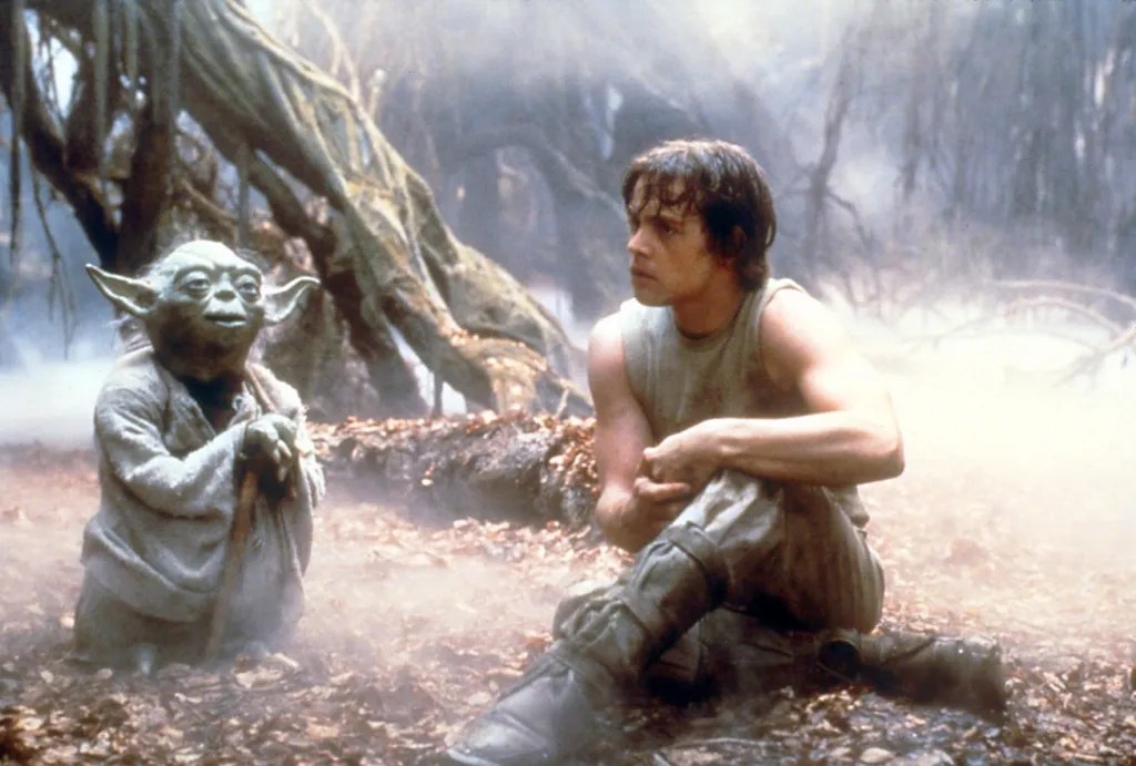 Yoda (voiced by Frank Oz) and Luke (Mark Hamill sitiing in a foggy swamp.
