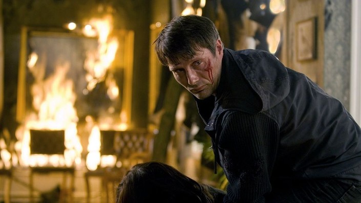 Thomas (Mads Mikkelsen)  leaning over his wife in a burning building.