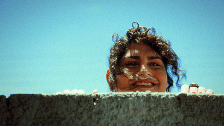 Madalena (Noá Bonoba) peeping smilingly over a wall. 