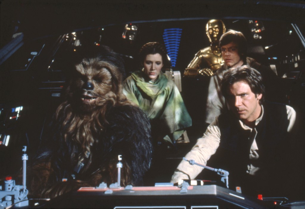 Chewbacca (Peter Mayhew) and Han (Harrison Ford) flying a space ship with Leia (Carrie Fisher) and Luke (Mark Hamill) behind them.
