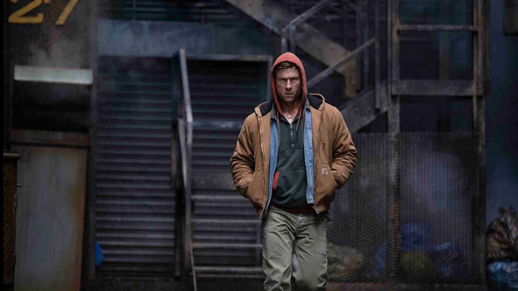 Ben Richards (Glen Powell) in a hoodie walking through an empty industrial area.