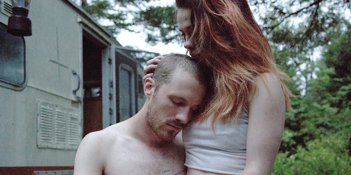 Blaise (Andrew Gillis) leaning against Nessa (Bhreagh MacNeil) who is stroking his head.