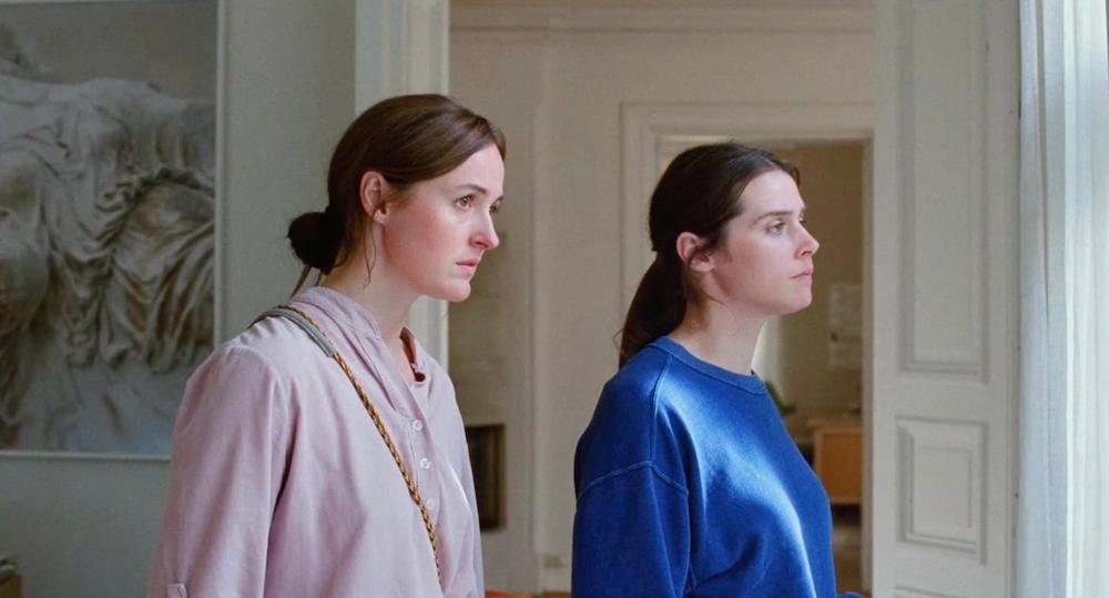 Nora (Renate Reinsve) and Agnes (Inga Ibsdotter Lilleaas) looking out a window in their family home together.