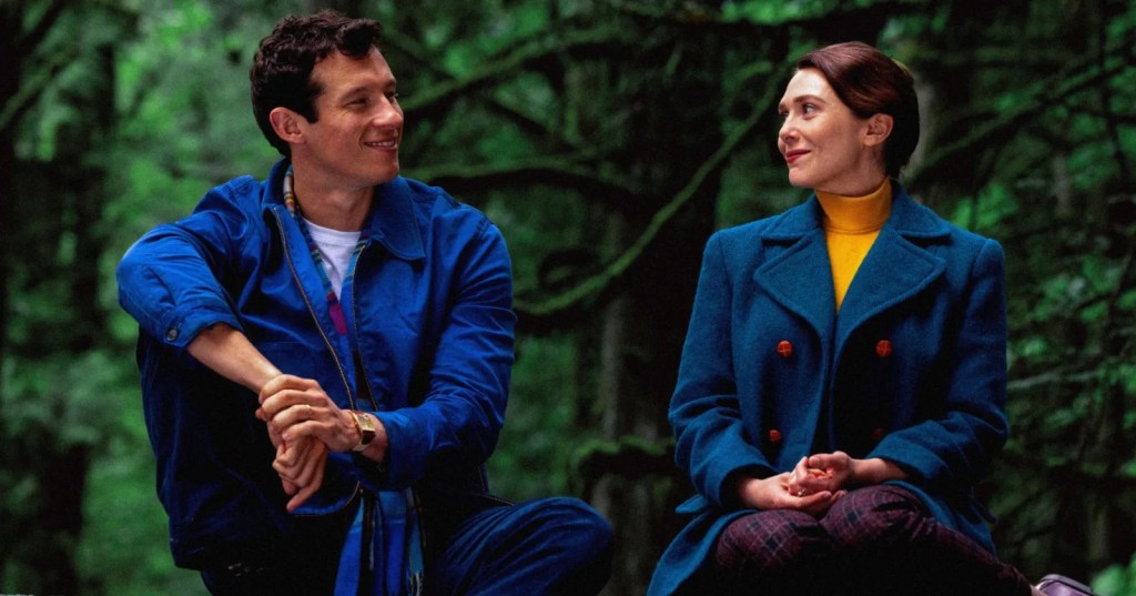 Luke (Callum Turner) and Joan (Elizabeth Olsen) sitting in a forest, smiling at each other.