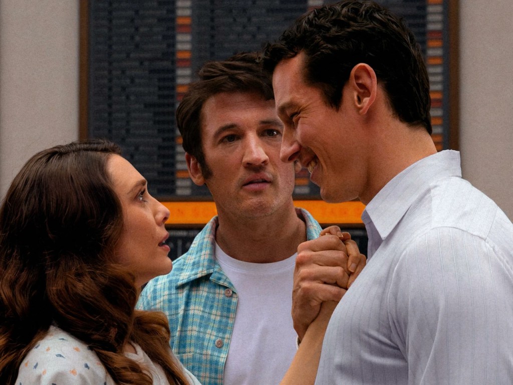 Luke (Callum Turner) and Joan (Elizabeth Olsen) looking at each other with joy and disbelief, their hands clutched together as Larry (Miles Teller) looks at Luke shocked.