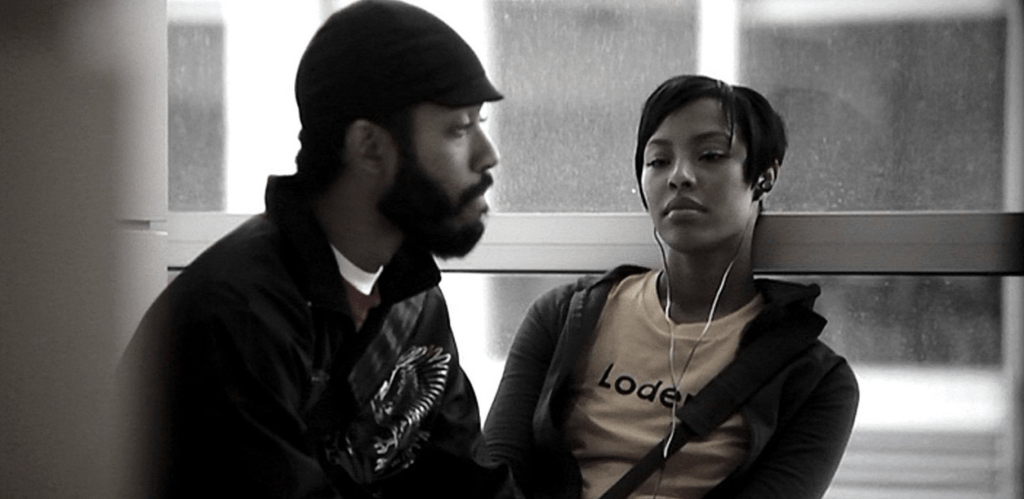 Micah (Wyatt Cenac) and Jo (Tracey Heggins) looking in different directions, she is wearing headphones.