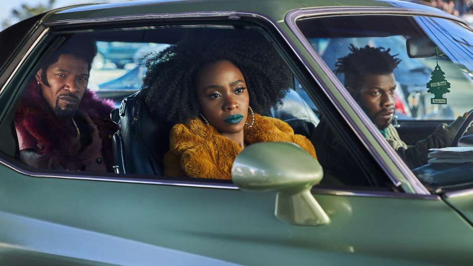 Slick Charles, Yo-Yo (Teyonah Parris) and Fontaine (John Boyega) sitting in a parked car, looking at something.