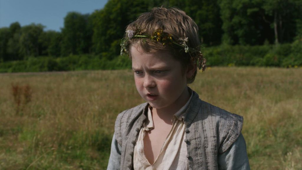 Hamnet (Jacobi Jupe) standing in a field, wearing a flower crown.