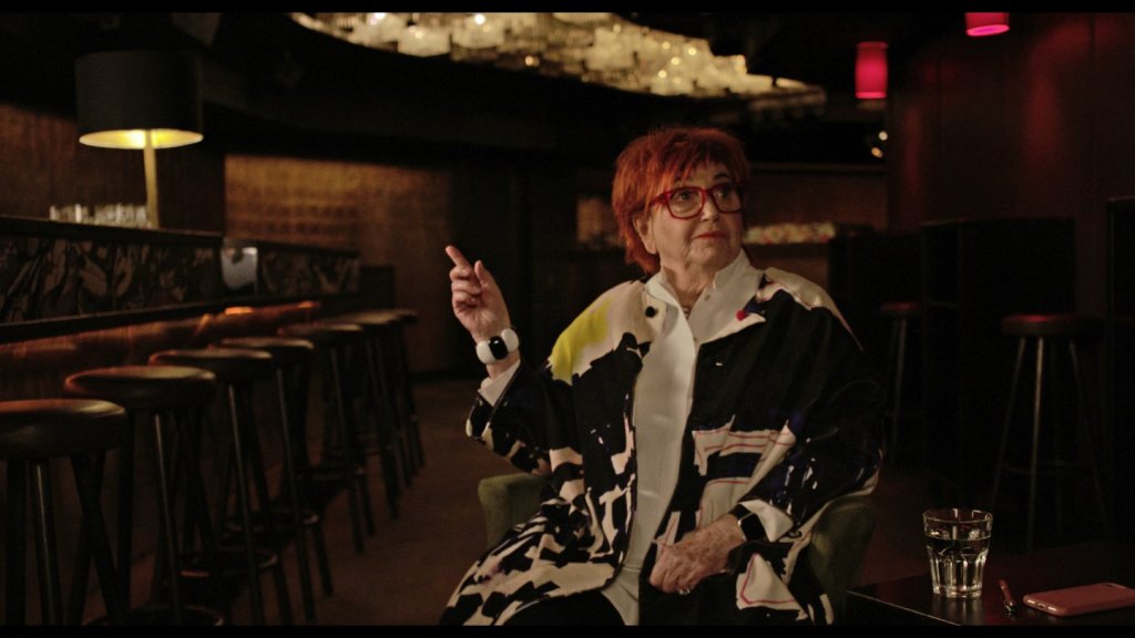 Valie Export, sitting in a bar, pointing at something.