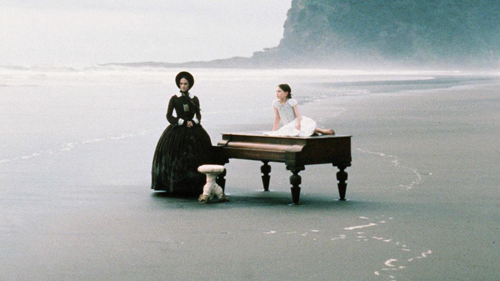 Ada (Holly Hunter) standing on a beach next to her piano. Her daughter Flora (Anna Paquin) is lying atop the piano. 