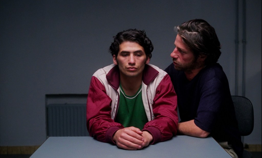 Erdal (Birol Ünel) sitting very close to Can (Tamer Yigit) in an interrogation room.  Can isn't looking at him.