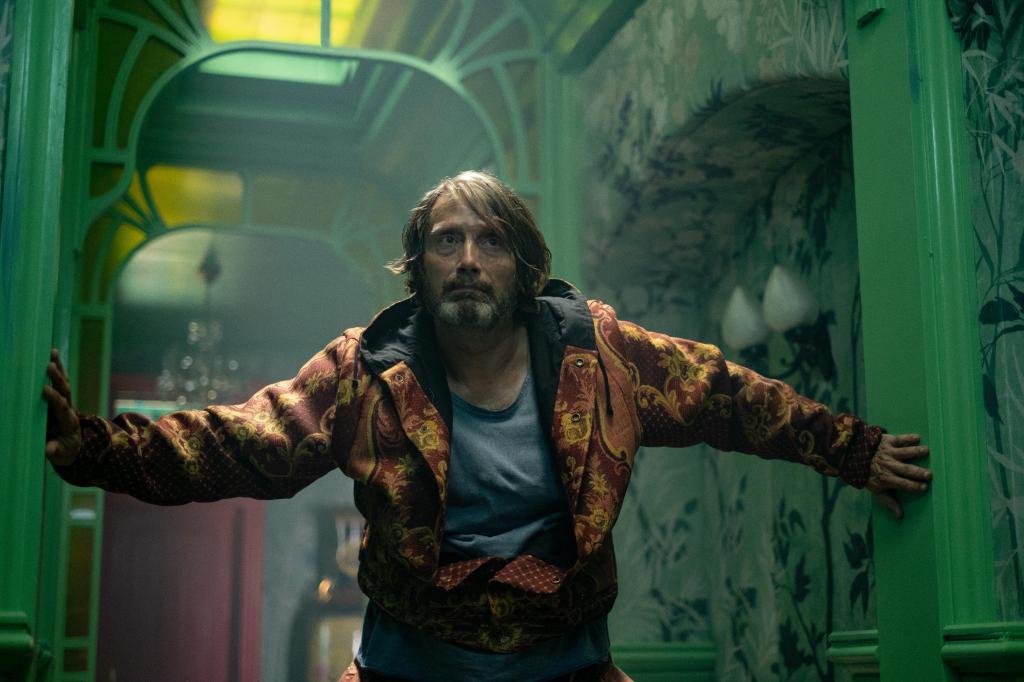 The neighbor (Mads Mikkelsen) bracing himself against a door frame in a hallway, looking a little bedraggled.