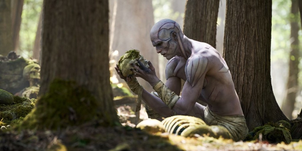 The Creature (Jacob Elordi) in the forest, holding up a moss-covered skull.