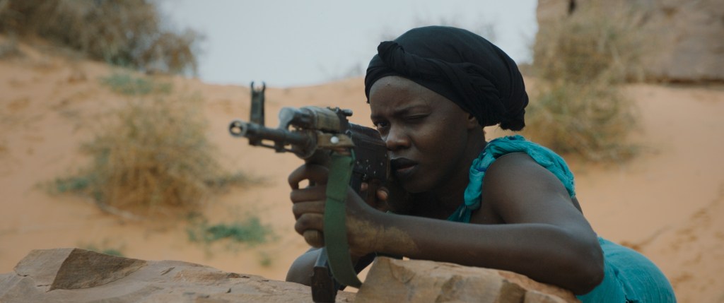 Sira (Nafisatou Cisse) aiming a machine gun.
