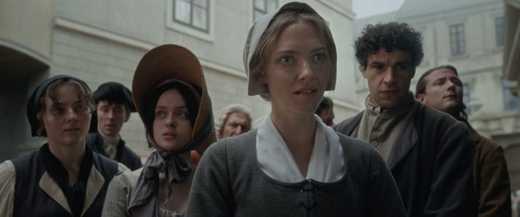 Ann Lee (Amanda Seyfried) standing in the streets of a city in the New World.