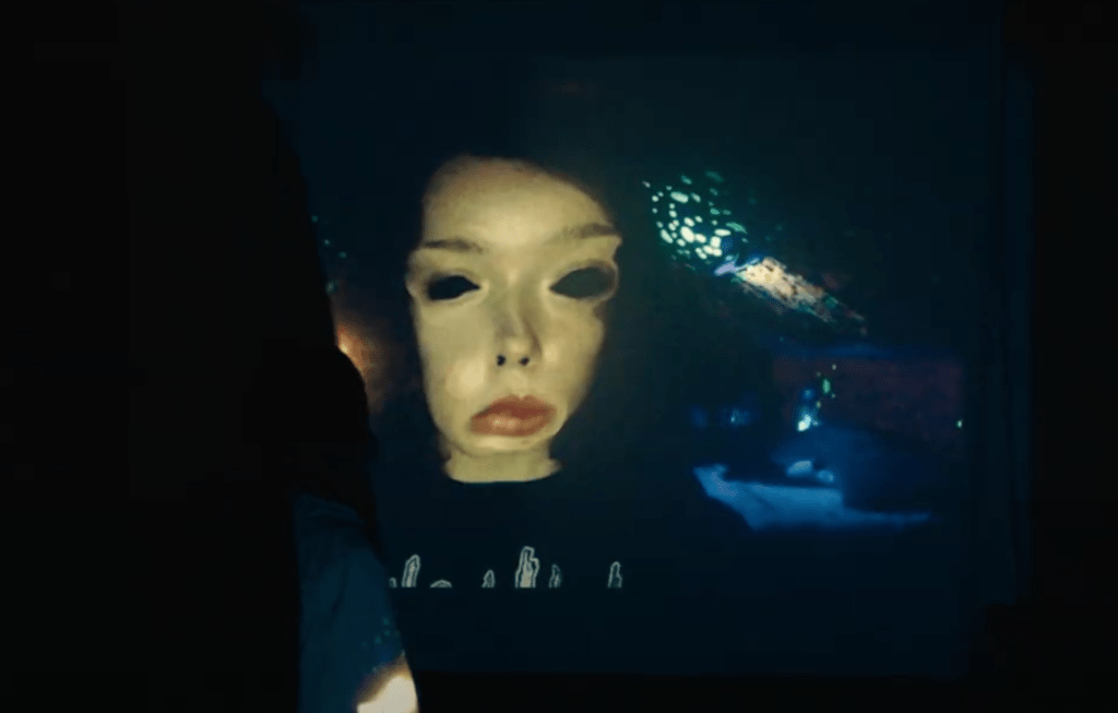 Casey (Anna Cobb) watching a video projected on a wall with a distorted version of her face from one of her own videos.