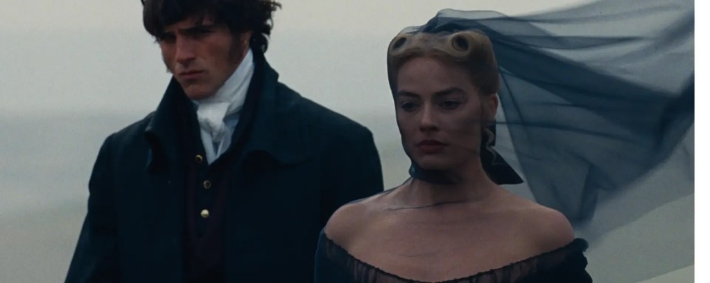 Heathcliff (Jacob Elordi) and Catherine (Margot Robbie) standing next to each other in mourning clothes.