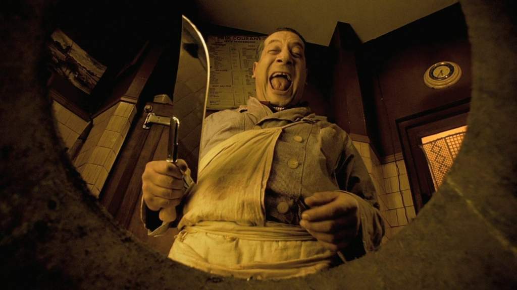 Clapet (Jean-Claude Dreyfus) holding a giant butcher knife and laughing, the camera is pointed at him from below, looking out of a trash can.