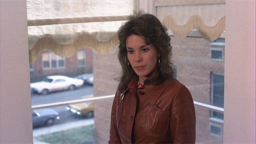 Grace (Jennifer Salt) standing in a bay window with a critical look on her face.