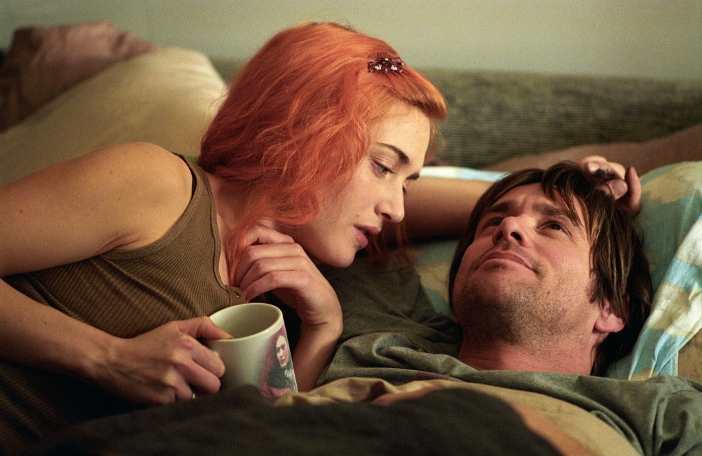 Clementine (Kate Winslet) with orange hair and Joel (Jim Carrey) lying in bed together, talking, cuddling.