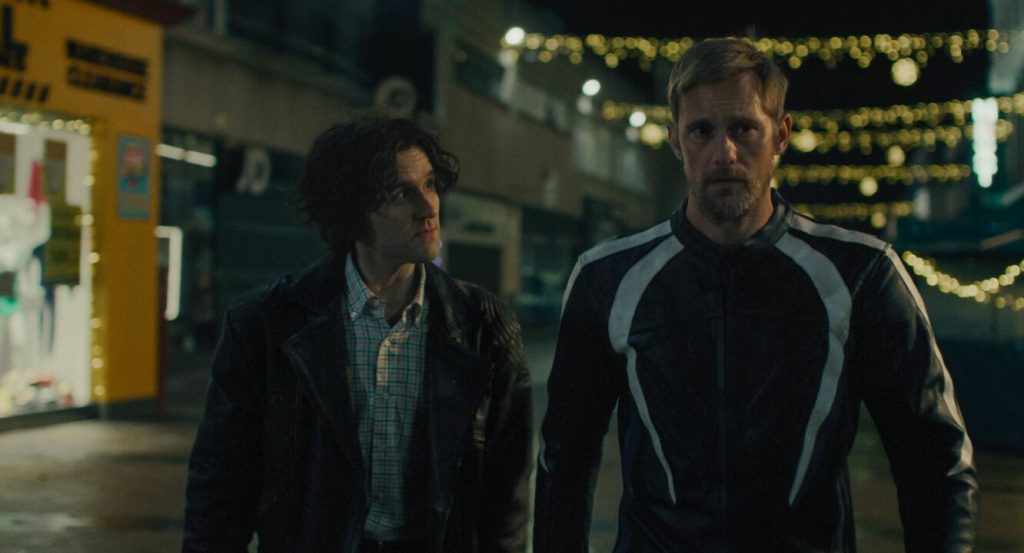 Colin (Harry Melling) and Ray (Alexander Skarsgård) walking through an empty city center strung with Christmas lights.