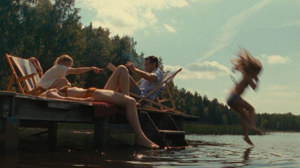 Lidia as a child jumping into a lake from a jetty on which her family is lounging.