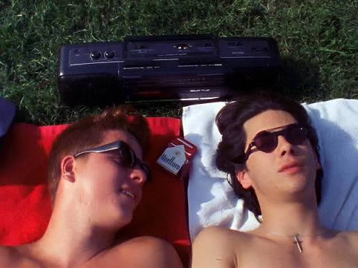 Tommy (Roko Belic) and Andy (James Duval) lying on the grass next to a ghetto blaster and a pack of cigarettes.