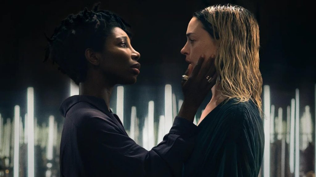 Sam (Michaela Coel) and Mary (Anne Hathaway) standing in front of some kind of vertical light installation. Sam is grabbing Mary's face, Mary has greasy hair and looks tired.