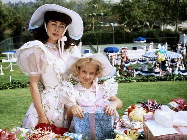 Joan (Faye Dunaway) and Christina (Mara Hobel) dressed to the nines in white dresses, posing with a bunch of birthday presents.