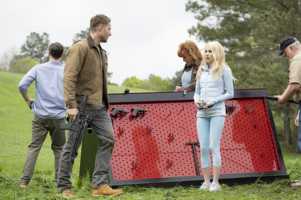 A group of people standing on a lawn next to cache of guns. They are all holdings gun. Some are obviously more confident with them than others.
