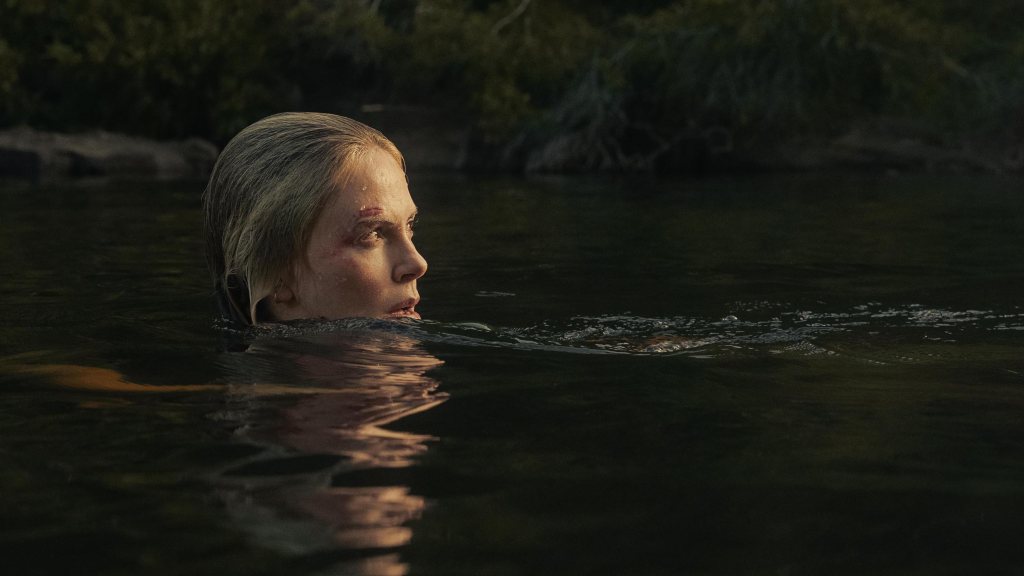 Sasha (Charlize Theron) in the water with just her head peeking out. She has a wound over her eye and glances backward suspiciously.