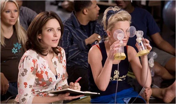 Kate (Tina Fey) and Angie (Amy Poehler) attending a birthing class together. Kate is taking notes. Angie is holding two breast pumps up to her eyes.