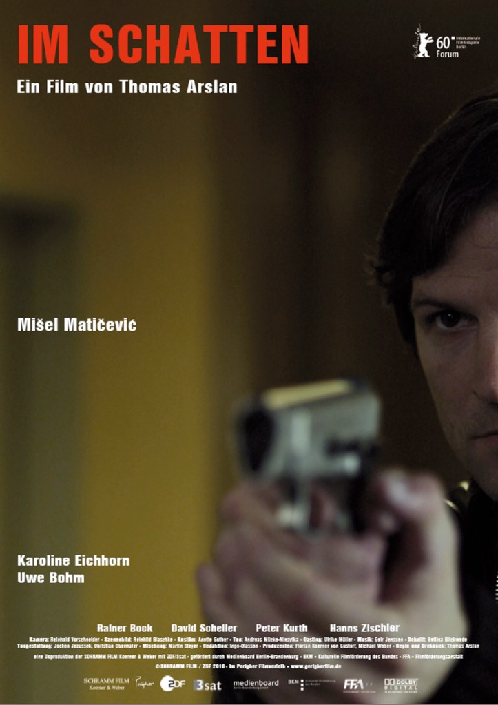 The movie poster showing half of Trojan's (Mišel Matičević) face and a gun he is aiming almost at the camera. His face is in focus, the gun blurry.