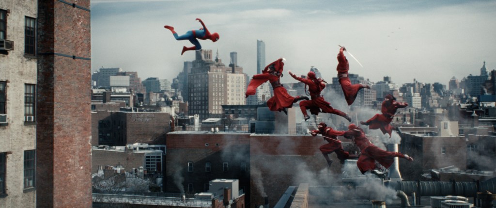 Spider-Man (Tom Holland) falling from a high building towards a group of red-clad assassins who in turn seem to be jump-flying towards him with raised weapons.